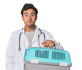 Young Hispanic man as vet with cage shrugs shoulders and open eyes confused.