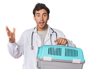 Young Hispanic man as vet with cage receiving a pleasant surprise, excited and raising hands.