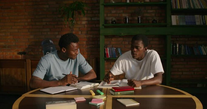 Two men are talking while studying the Bible together. They are sitting at the table indoors