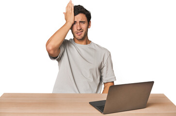 Hispanic young man working on laptop forgetting something, slapping forehead with palm and closing...