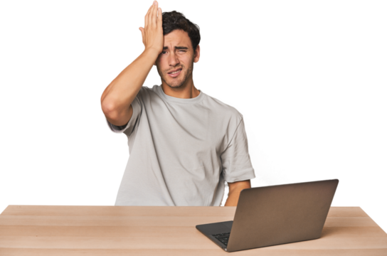 Hispanic young man working on laptop forgetting something, slapping forehead with palm and closing eyes.