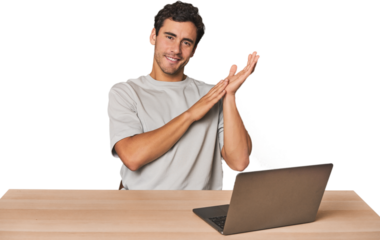 Hispanic young man working on laptop feeling energetic and comfortable, rubbing hands confident.