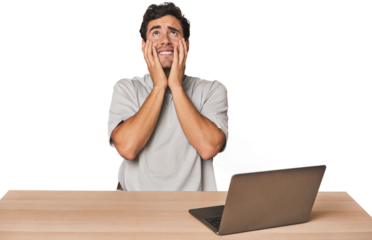 Hispanic young man working on laptop whining and crying disconsolately.