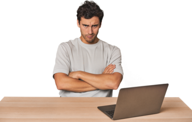 Hispanic young man working on laptop unhappy looking in camera with sarcastic expression.