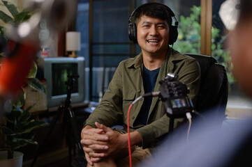 Two hosts of podcasts a happy radio host in a chic studio, one speaking into the microphone as the other listens intently while donning headphones to record a podcast.