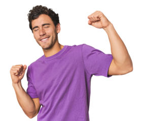 Young Hispanic man in studio celebrating a special day, jumps and raise arms with energy.