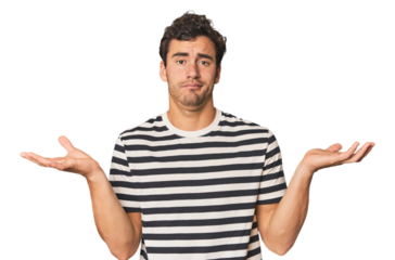 Young Hispanic man in studio doubting and shrugging shoulders in questioning gesture.