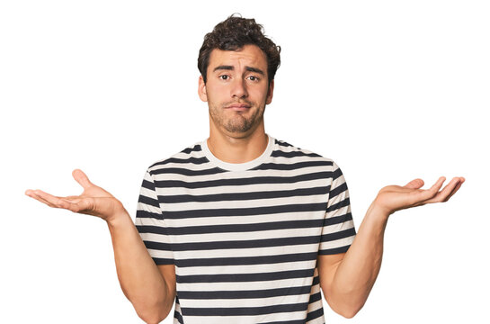Young Hispanic man in studio doubting and shrugging shoulders in questioning gesture.