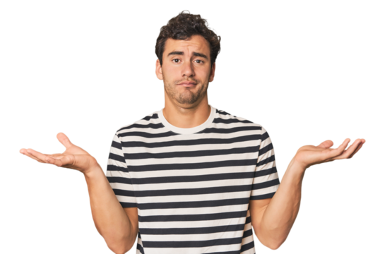 Young Hispanic man in studio doubting and shrugging shoulders in questioning gesture.