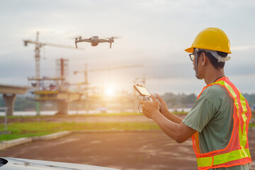 An Asian engineer using a drone to survey the location of a large concrete bridge that will link two roads To inspect equipment on construction sites, technicians use drones rather than workers.