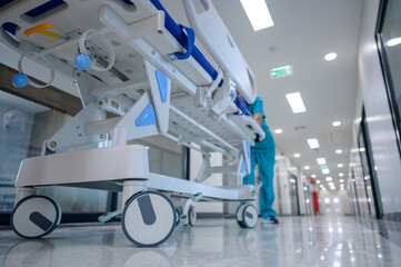 A hospital bed trolley being pushed down a clean, white hallway as other hospital bed trolleys push patients