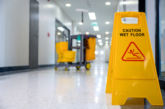 Focus on yellow wet floor warning sign and caution slippery sign background of cleaning using mop mopping the floor cleaning in office with cleaning cart and floor cleaning tools and equipment
