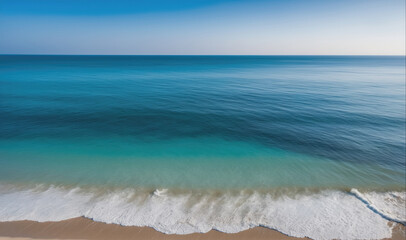 A serene aerial view of the ocean and beach on a bright, sunny day. The turquoise water crashes into the sandy shore, creating a beautiful contrast