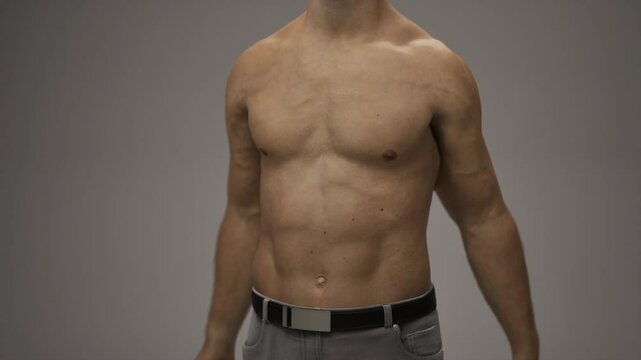 A man without a shirt confidently poses for a picture, showcasing his muscular build and defined physique in a casual setting.