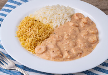 Shrimp strogonoff with rice and straw potato over wooden table