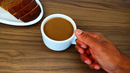 Hand holding cup of coffee with milk known as latte on the wooden table with copy space.	
