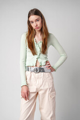 Woman in Green Cardigan and Beige Cargo Pants Poses Against a White Wall