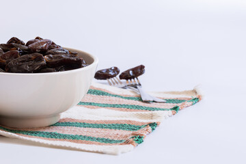 Bowl with dried dates on the left of the image and two forks with dates out of focus on the right of the bowl