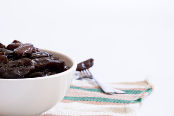 Bowl full of dried dates on the left of the image and fork with date out of focus on the right of the bowl