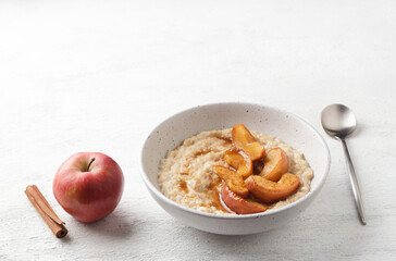 Sweet oatmeal porridge with baked apple slices, cinnamon and caramel sauce in a gray bowl on a light background