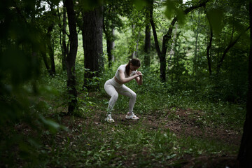 Young caucasian woman in white sportswear exercising in green forest park