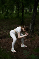 Young caucasian woman in white sportswear exercising in green forest park