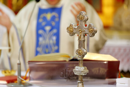 Holy Cross with Jesus Christ on the altar during the Holy Mass, the priest in the background and empty space for text.