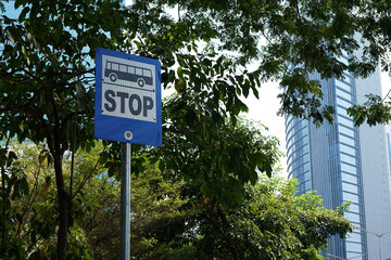 Bus Stop sign under trees with high rise buildings in the background              