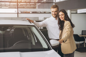 It is the one car I want! Beautiful young couple standing at the dealership choosing the car to buy