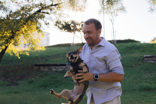 Smiling middle-aged man walks and plays with a small dog in public park