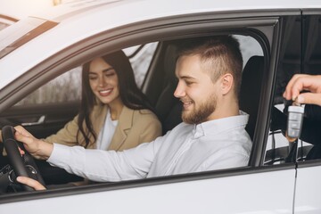 Happy couple buying car in huge showroom, taking automobile key from young handsome salesman while sitting inside auto. Cheerful arab man and woman purchasing beautiful vehicle, closeup