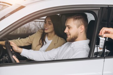 Happy couple buying car in huge showroom, taking automobile key from young handsome salesman while sitting inside auto. Cheerful arab man and woman purchasing beautiful vehicle, closeup