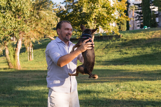 Smiling middle-aged man walks and plays with a small dog in public park