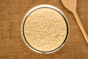 Round-grain rice in a glass jar with a wooden spoon on a jute cloth, macro, top view.
