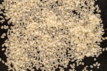 Round grain uncooked rice on slate stone, macro, top view.