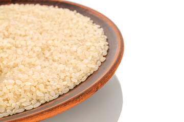Round grain uncooked rice in a clay plate, macro, isolated on white background..