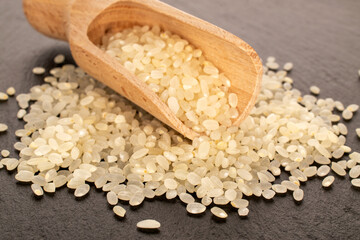 Round grain uncooked rice with wooden spoon on slate stone, macro.