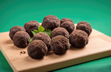 A group of chocolate truffles sit on a wooden cutting board