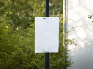 Empty election poster mockup. Template for an ad placard at a street mounted to a lamp post. Blank advertisement space in front of green leaves.