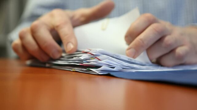 Businessman sitting at desk in office looking through folder with documents. Macro.