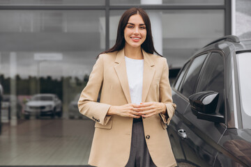 Happy woman customer female buyer client in beige jacket hold hands crossed folded choose auto want to buy new automobile in car showroom vehicle salon dealership store motor show indoor.