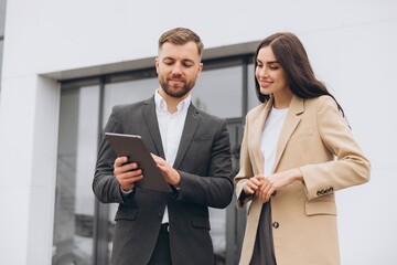 Bearded business man car salesman in grey suit giving explanations on tablet to pretty young woman...