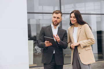 Bearded business man car salesman in grey suit giving explanations on tablet to pretty young woman...