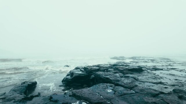 Very mist and foggy scene on the coast of the UK. Winters coastal seascape with small boats and rough seas crashing against the rocks and cliffs on the east coast of the UK. English cold spell