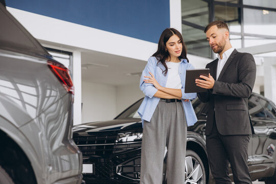 Young woman customer female buyer client wears shirt consult with salesman hold tablet choosing auto want to buy new automobile in car showroom vehicle salon dealership store motor show.