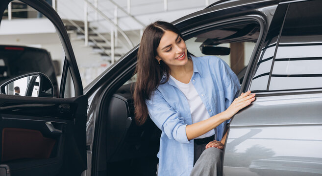 Happy friendly woman customer female buyer client wears blue shirt stand inside car chooses auto wants to buy new automobile in showroom vehicle salon dealership store motor show indoor.