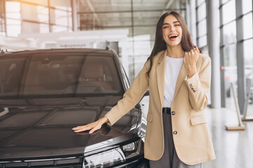 Charming young Caucasian woman hugging hood of new car and show fist and say yes in modern bright...
