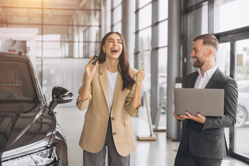 Charming young Caucasian woman holding keys of new car and show fist and say yes in modern car...