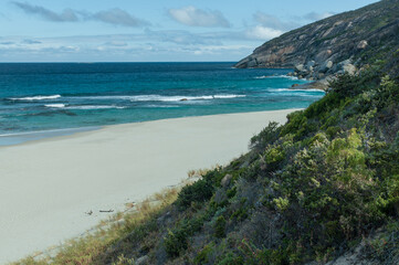 Turquoise waters meet pristine white sand at a secluded beach in Western Australia. Rugged coastline and scattered boulders create a picturesque and tranquil coastal escape.