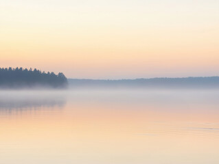 Fototapeta premium A peaceful lake at sunrise, shrouded in mist, reflects the soft morning light. A distant forest silhouette adds to the tranquil atmosphere. 